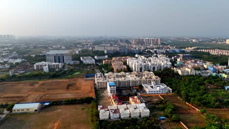 this aerial view shows a developing urban area. in the foreground is open, undeveloped land next to new mid-rise residential buildings. beyond these a denser city landscape stretches to a hazy horizon
