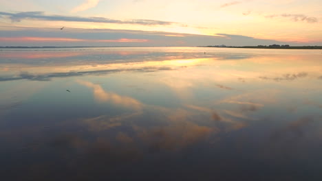 sunset over sea with flying bird along drone with reflections in water
