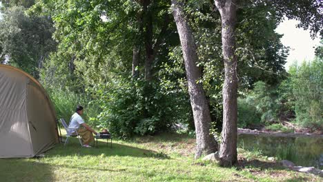 an asian girl camping alone by the river, lost in thought