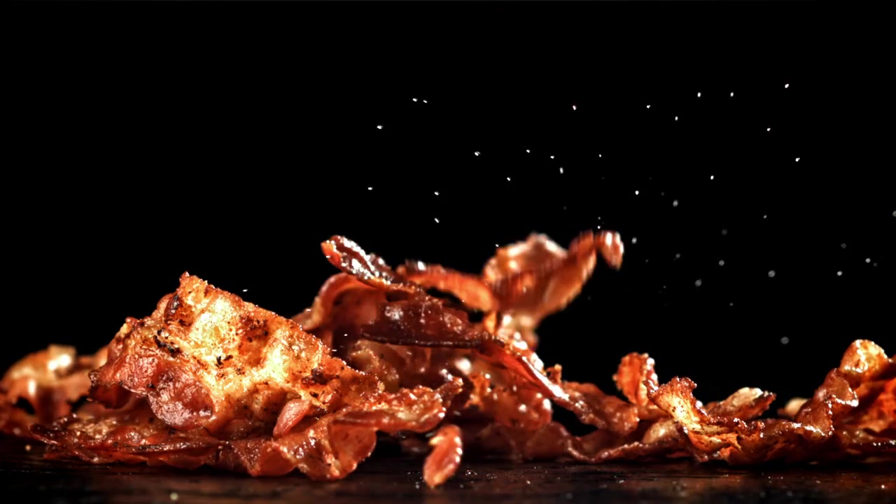 Sprø baconstrimler faller i sakte film på svart bakgrunn