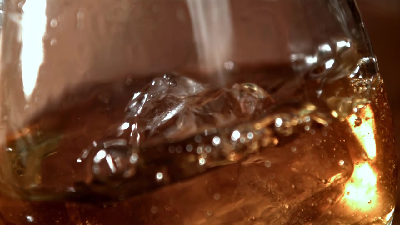Versamento di whisky al rallentatore in un bicchiere con ghiaccio