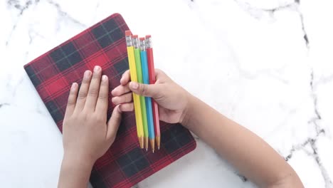 manos sosteniendo lápices de color en la parte superior de un cuaderno de cuadros rojos