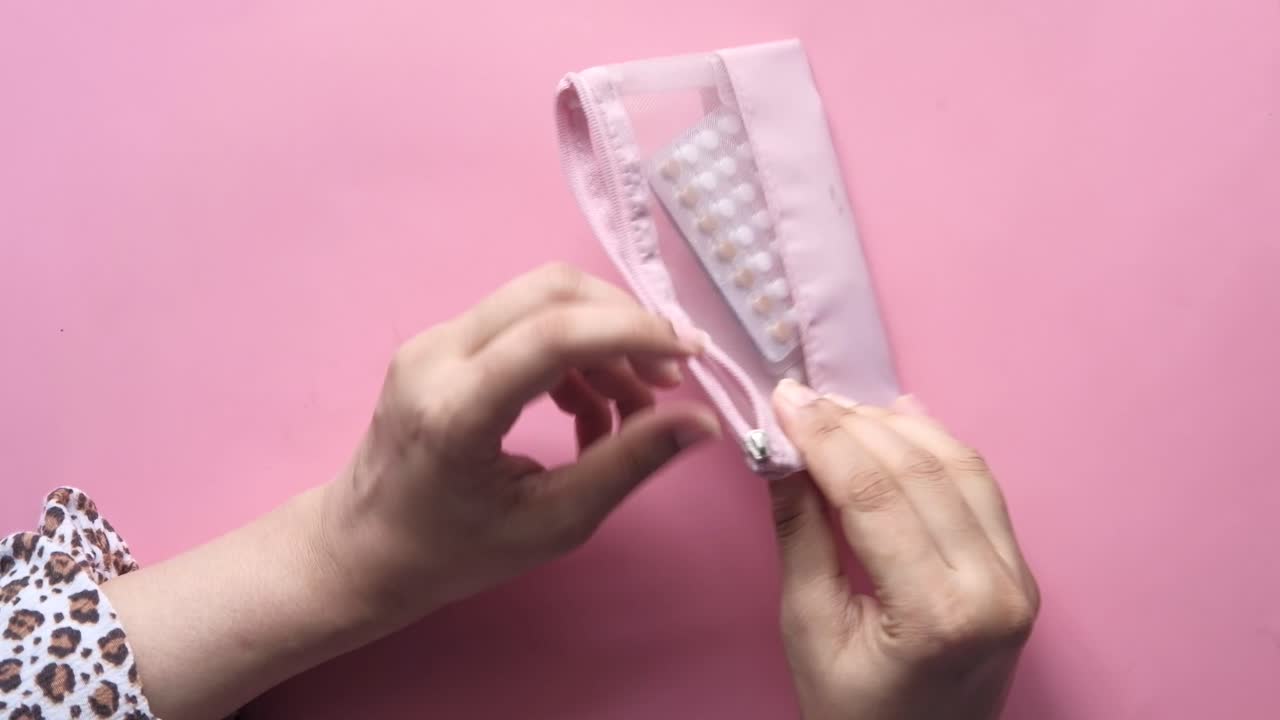 Manos de mujer abriendo un estuche rosa con cremallera que contiene píldoras