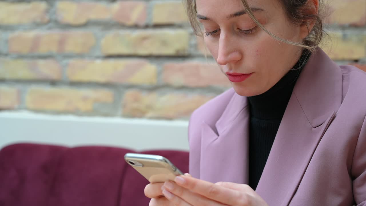 Close up of a woman in a pink blazer typing on her phone in a restaurant