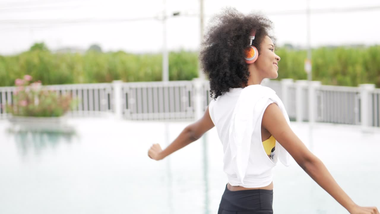 mujer africana en ropa deportiva con auriculares bailando en el fondo de la piscina.