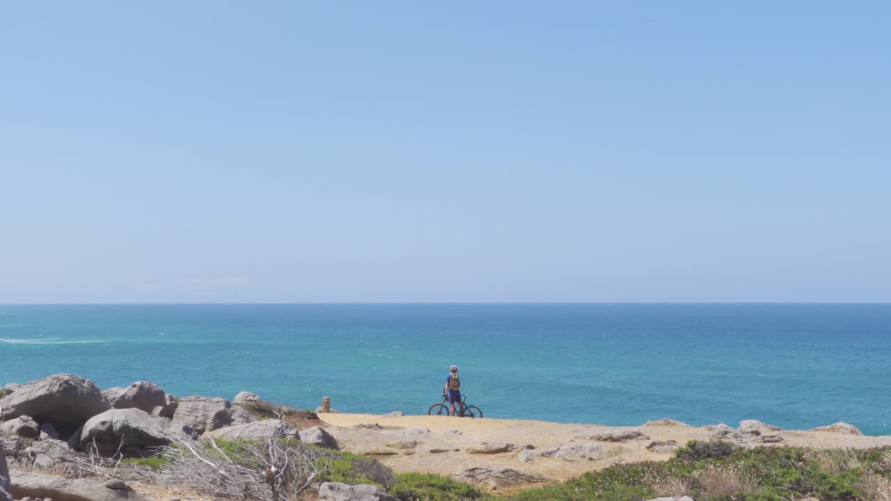 절벽 옆에서 푸른 대서양의 경치를 즐기다가 다시 자전거를 타는 자전거 타는 사람