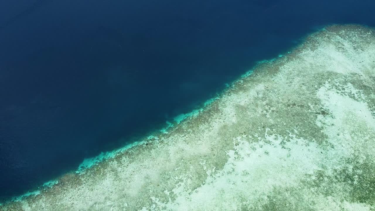 Shallow, crystal clear water transitioning to deeper blue ocean and coral reef in Raja Ampat, West Papua, Indonesia, aerial drone view