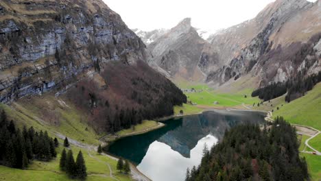 sobrevuelo aéreo junto a seealpsee en appenzell, suiza, que revela un reflejo de los picos alpstein en el lago detrás de los árboles