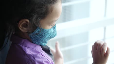 child wearing a face mask looking out a window