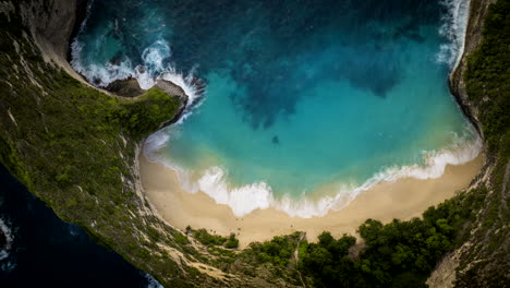 Ocean-waves-crash-on-golden-sandy-beach-cove-of-Keling-King,-aerial-time-lapse