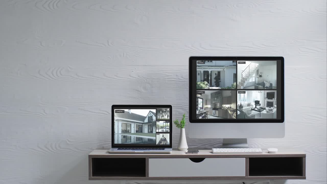 Wall mounted computer monitor and laptop on desk with security camera views on screens, slow motion