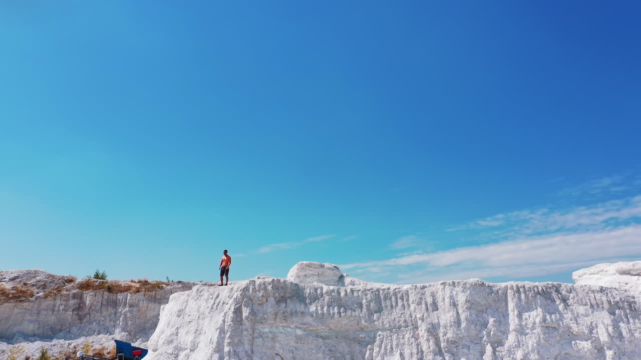 Drone view on a sporty man in canyon. Sportsman in shorts standing on the edge of the white hill in a bright summer day. Aerial view.