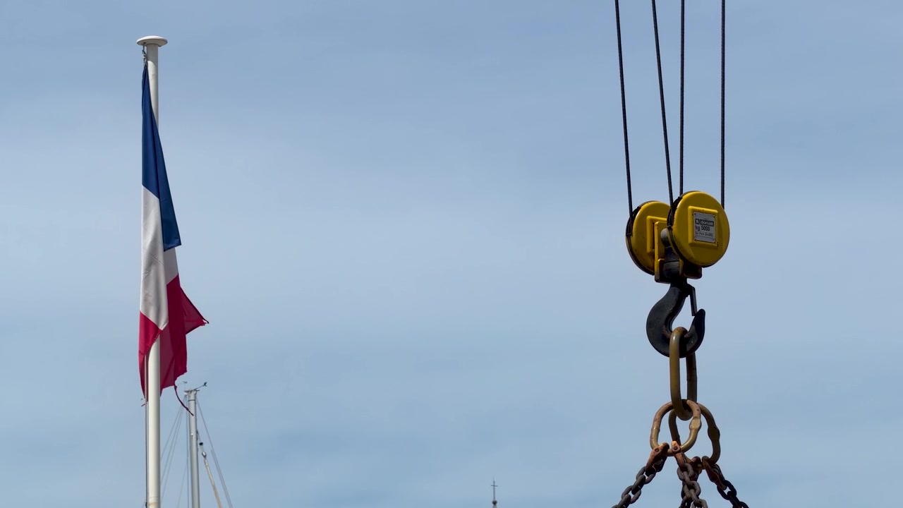 Et fransk trefarvet flag vajer i vinden ved siden af en industriel krankrog.