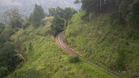 aerial shot of curving train track in the middle of a forest hill and man walking