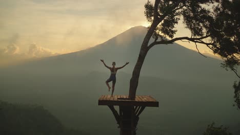 fit female doing tree pose on view platform looking at mount agung with mist, sunset