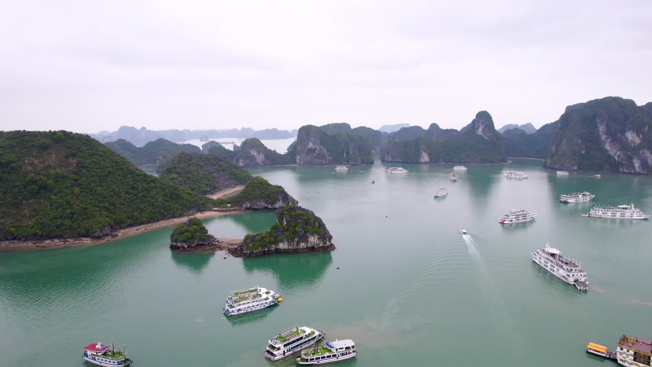 Luchtfoto, dolly, kalm smaragdgroen water bezaaid met kalkstenen karsteilanden en voor anker liggende veerboten, mistige bewolkte dag, Ha Long Bay Vietnam