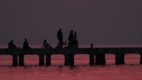 family silhouettes fishing at sunset pier