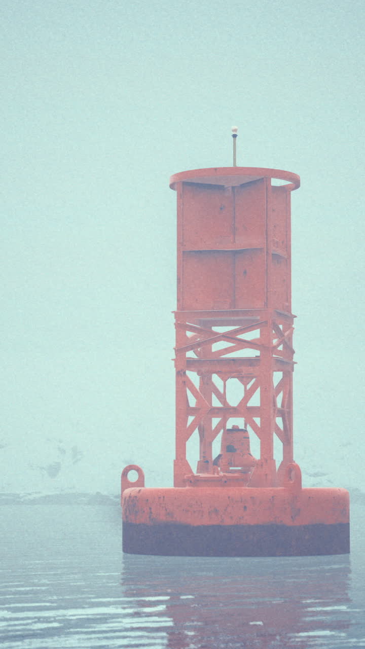 Bright orange buoy stands alone in foggy waters near a snowy landscape