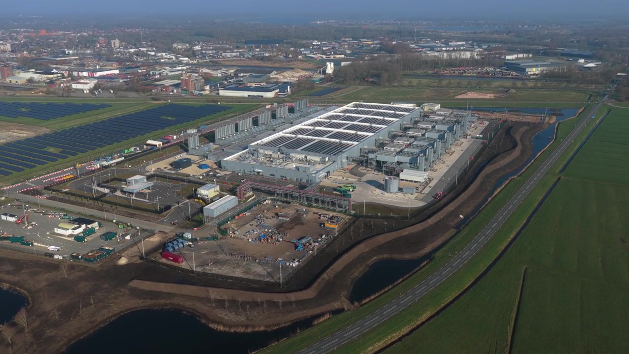 Ampia prospettiva aerea di un moderno data center di cloud computing AI in costruzione, adiacente a un grande parco solare a Winschoten, Paesi Bassi.