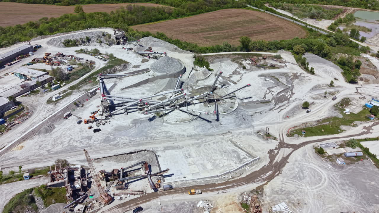 Construction site shows heavy machinery and workers engaged in building operations near a quarry during daylight hours in a rural area