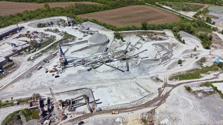 Construction site shows heavy machinery and workers engaged in building operations near a quarry during daylight hours in a rural area