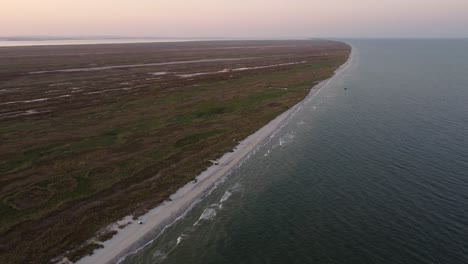 Vista-Panorámica-Aérea-Al-Atardecer-Del-Mar-Negro-Que-Se-Encuentra-Con-La-Playa-Salvaje-Llena-De-Vegetación-Natural-En-Rumania,-Europa