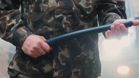 a man in camouflage with a rubber baton beats his arm