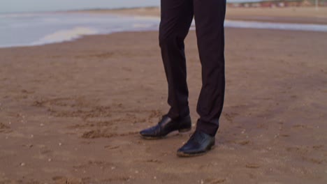 A-male-man-black-latino-model-in-a-suit-walks-on-the-beach-and-takes-off-his-belt-at-the-seashore-with-sunglasses-in-the-Netherlands,-the-Hague