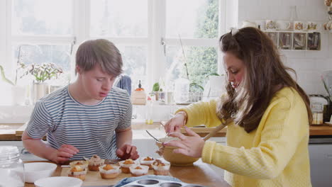 young downs syndrome couple decorating homemade cupcakes with icing in kitchen at home