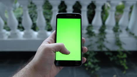 close up shot of man hand scrolling with smartphone, garden with plants on background