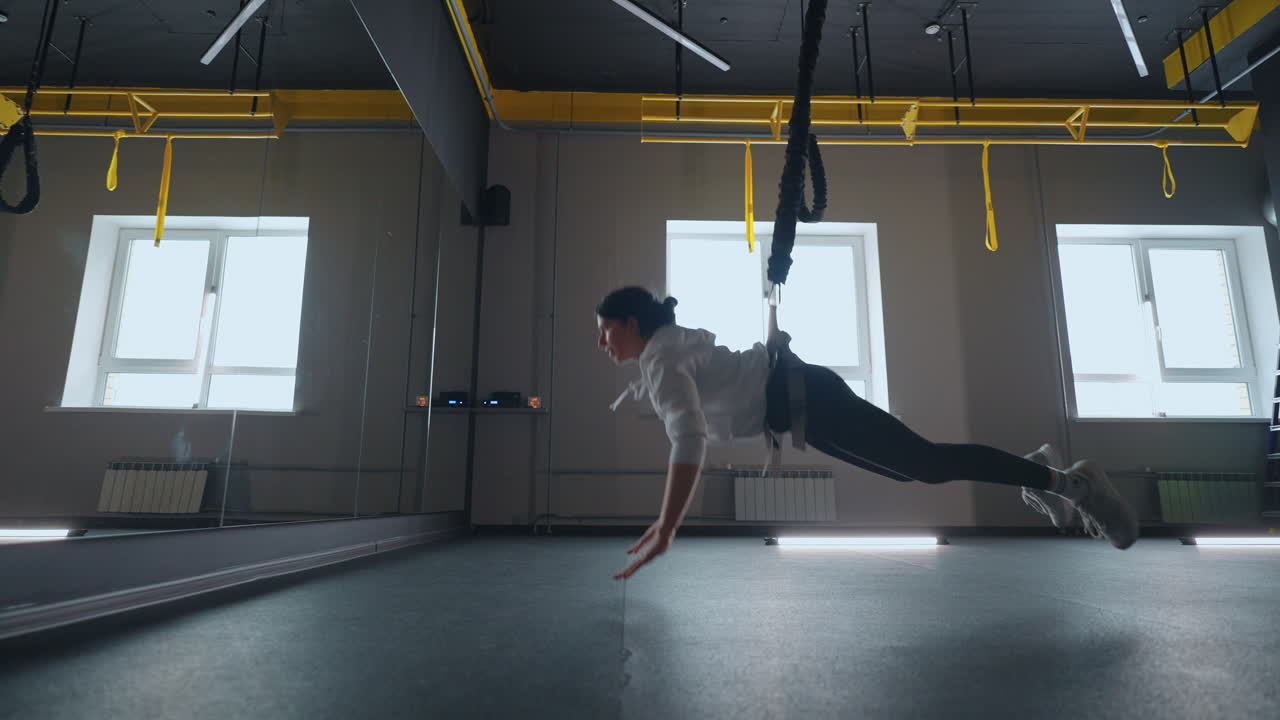 entrenamiento deportivo con sistema moderno de trx en el gimnasio joven mujer atlética está haciendo saltos con suspensión