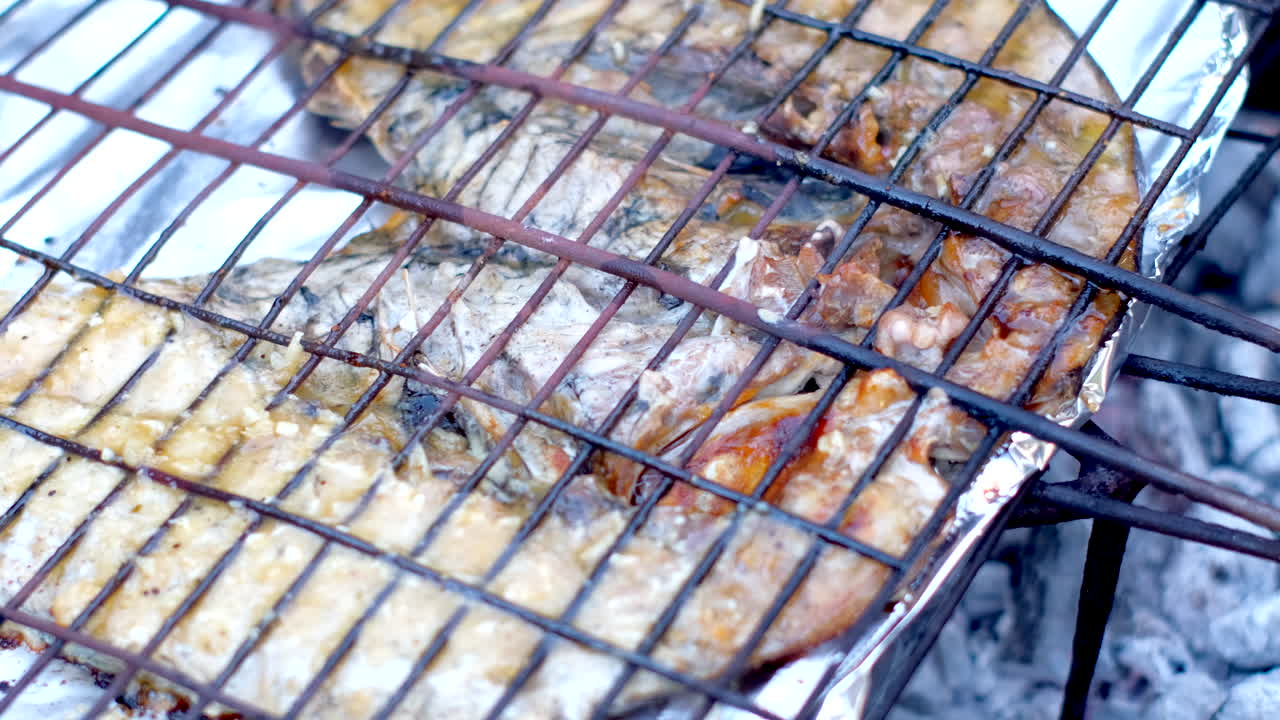 Pesce sarago nero succulento sulla griglia, cotto su carboni ardenti, vista ravvicinata.