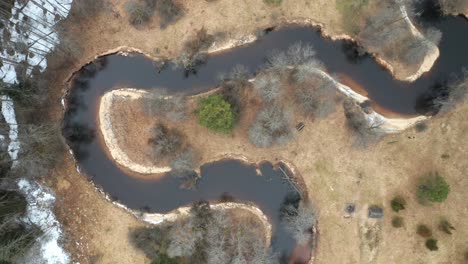 AERIAL:-River-Flows-Near-Forest-with-Part-of-it-Covered-in-Snow