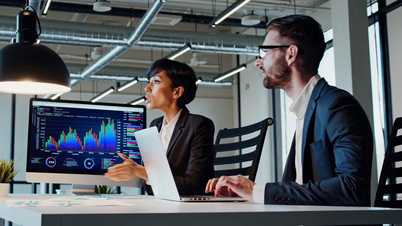 A side-angle video of two professionals analyzing data on a computer screen in a modern office