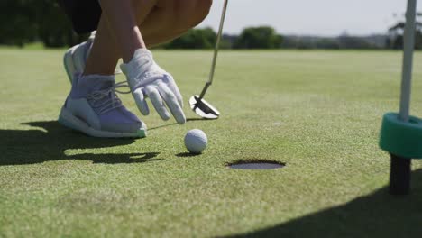 caucasian woman playing golf reaching for a ball