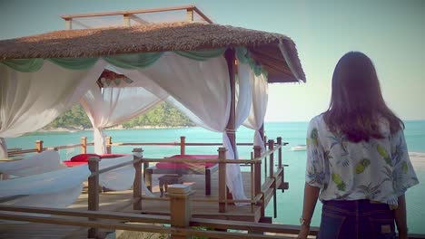 girl is standing by the railing next to the gazebo for a massage on a rocky cliff with sea view