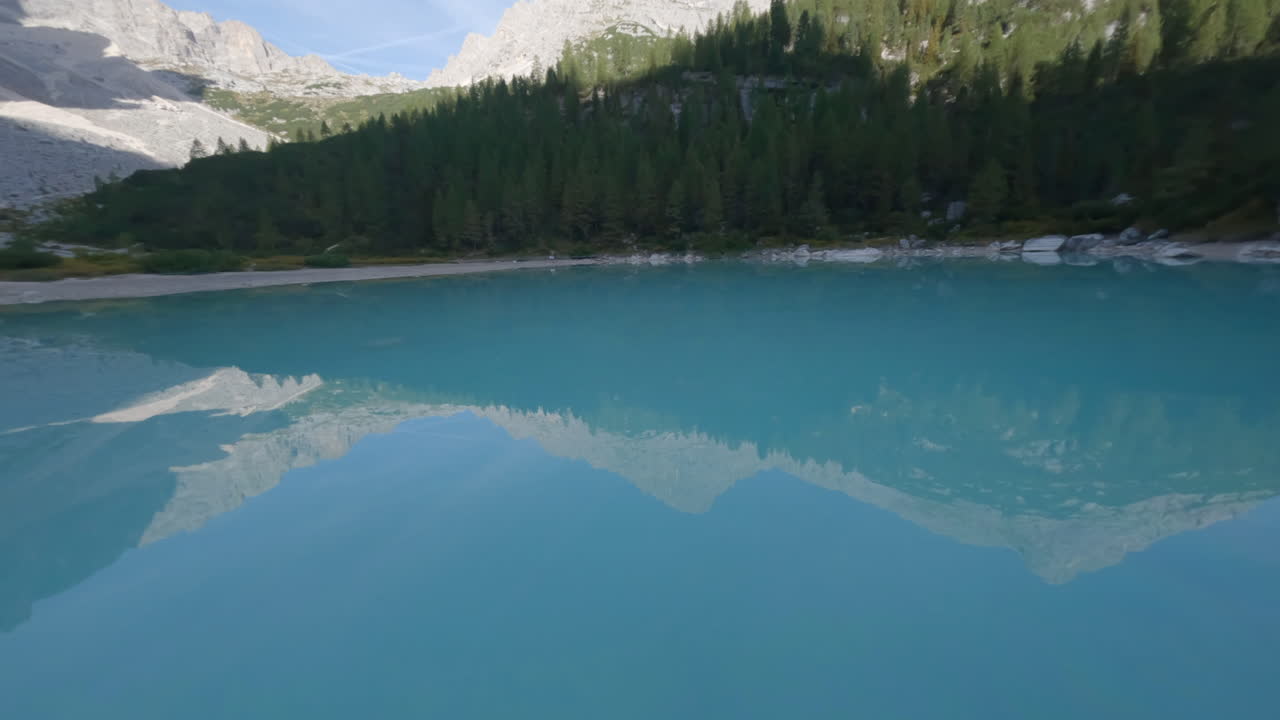 drone fpv acelerando a través de impresionante lago alpino azul que refleja las montañas italianas dolomitas reflejadas en la superficie de las aguas