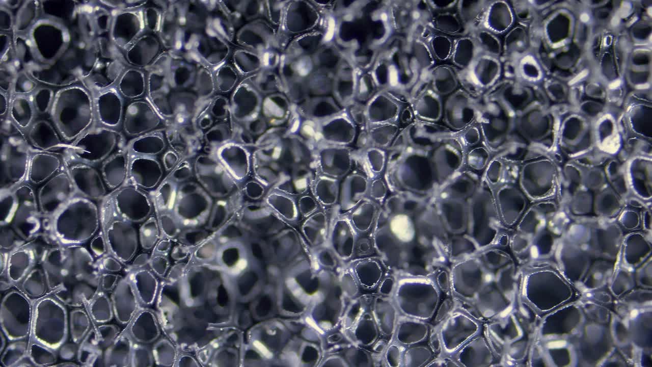 Black, open-cell polyurethane sponge structure under microscope