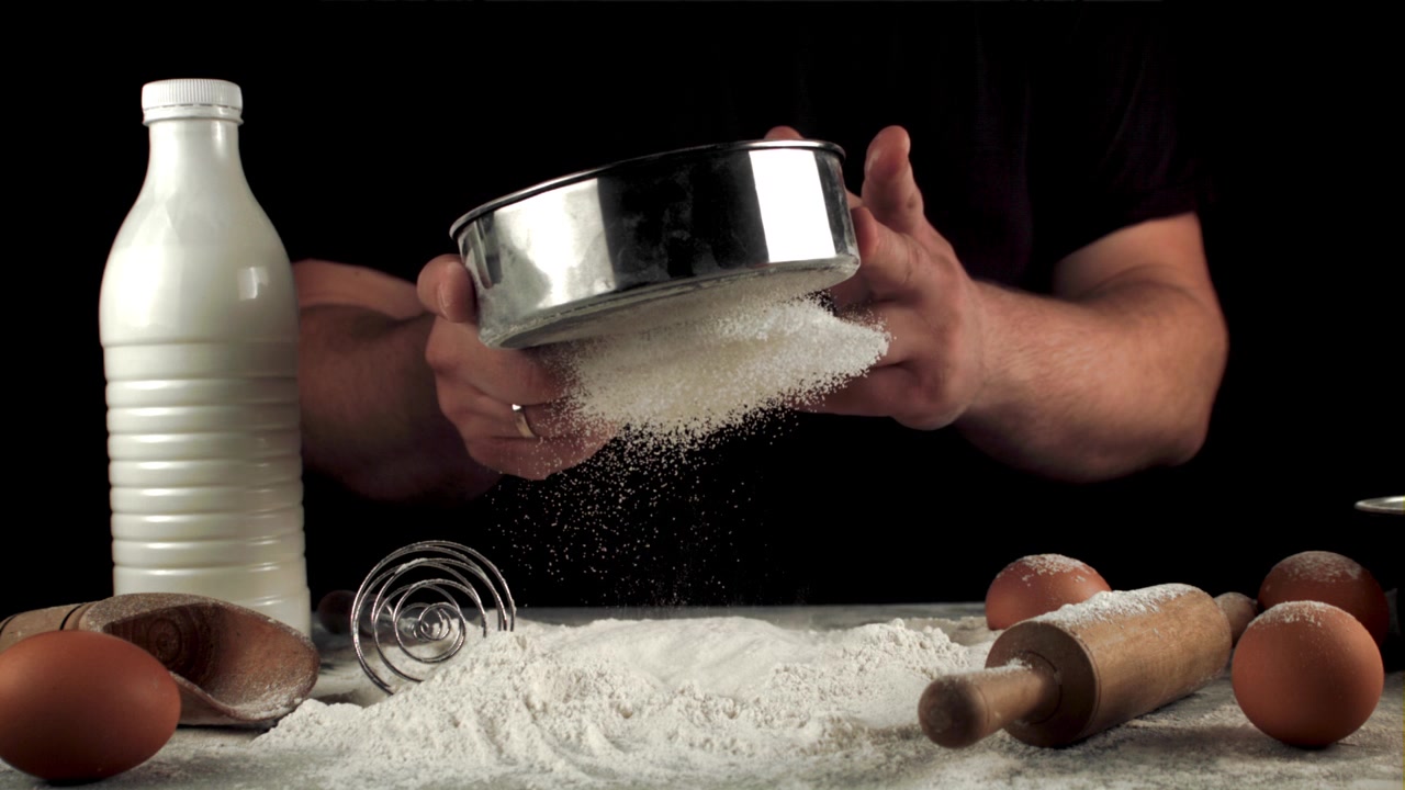 Nærbilde av hender som sikter mel til baking