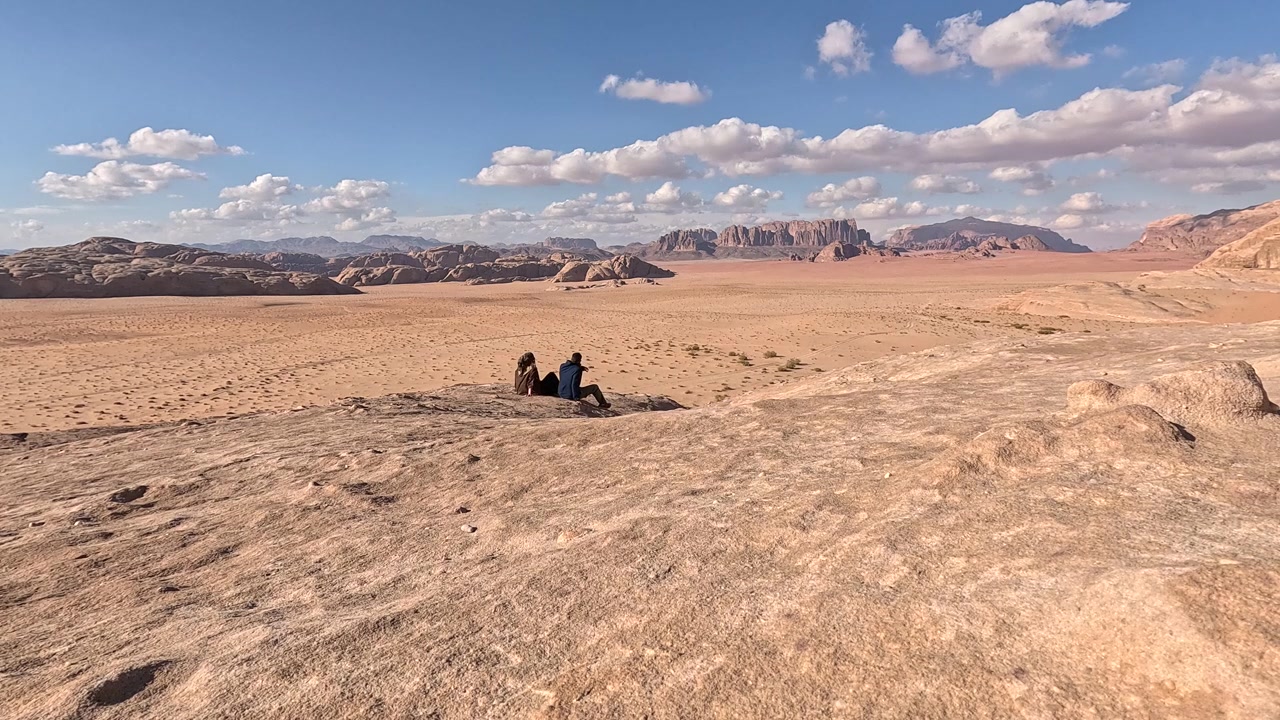 Breathtaking footage of a couple walking along a dramatic cliff edge high above the vast red desert landscape of Wadi Rum, soaking up the extraordinary otherworldly scenery of one of Jordan's most ico