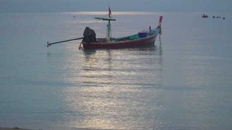 a longtail boat anchored in the calm waters of a tropical beach at sunset