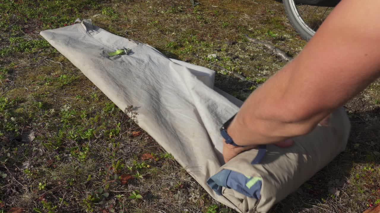 Et telt rulles forsiktig sammen og pakkes på bakken, forbereder seg på neste etappe av en campingtur i Norge - nærbilde