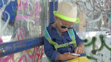 niño con teléfono inteligente en la parada de autobús de la ciudad de grungy