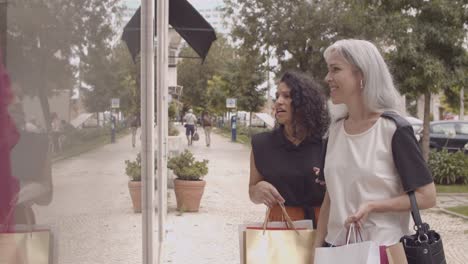 happy female friends standing outside, looking the store