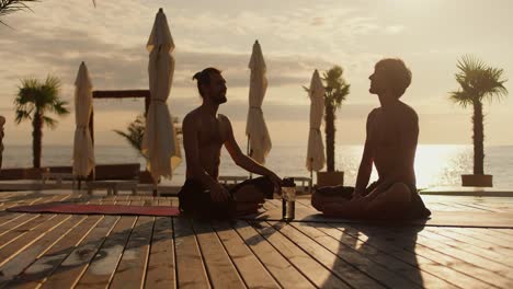 Zwei-Männer-Sitzen-Morgens-Auf-Matten-Und-Unterhalten-Sich-Am-Strand.-Entspannen-Sie-Sich-Bei-Sonnenaufgang-Am-Sonnigen-Strand