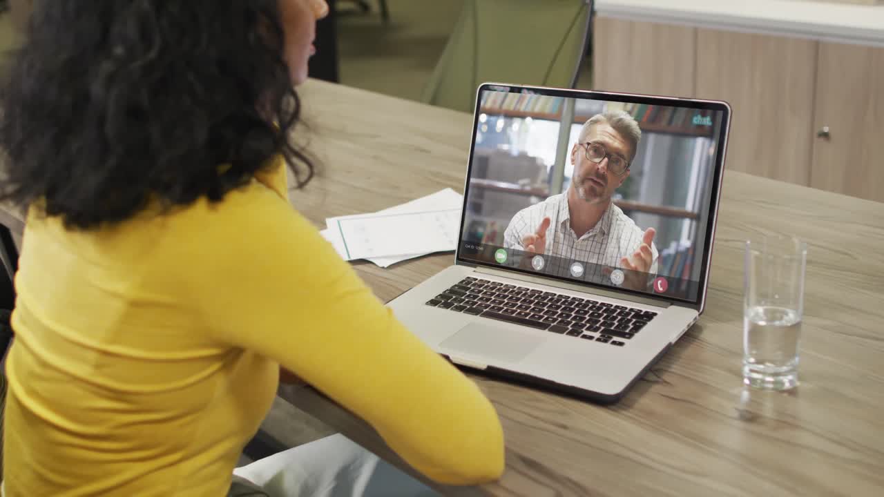 video de una mujer afroamericana haciendo una videollamada en una computadora portátil con un compañero de trabajo caucásico