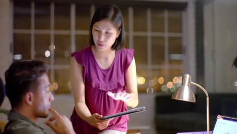 focused diverse male and female colleague discussing work using tablet and laptop at night in office