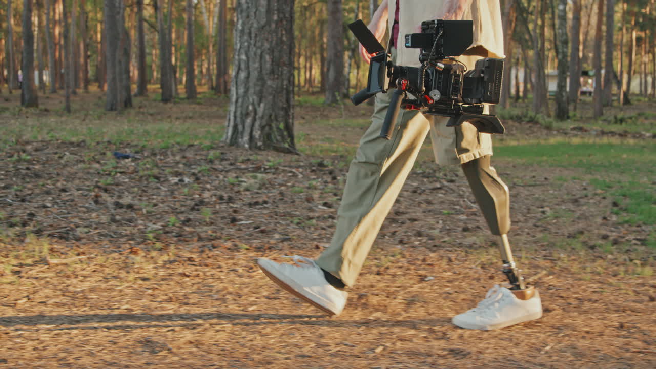 Cameraman With Robotic Leg Walking In Forest With Video Camera