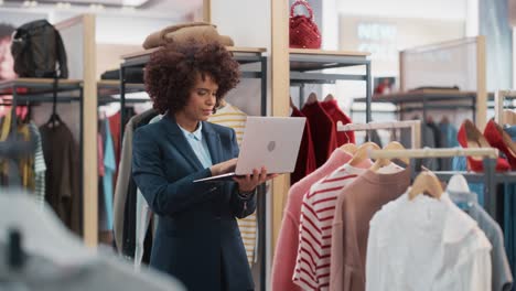 clothing store: female merchandising manager uses laptop computer to create stylish fashion collection. professional shop sales retail assistant checks stock. small business owner orders mall items.