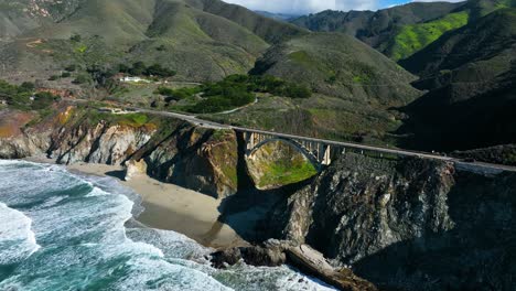 luftaufnahme der rocky creek bridge, wellen, die unten am ufer gegen die grüne bergkette schlagen, highway 1 in kalifornien